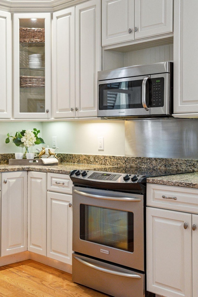 kitchen featuring white cabinets, stone counters, appliances with stainless steel finishes, and light hardwood / wood-style flooring