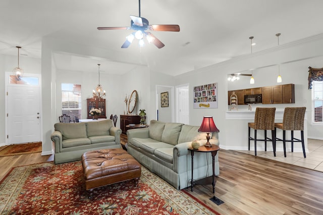 living room with plenty of natural light, ceiling fan with notable chandelier, light wood-type flooring, and baseboards