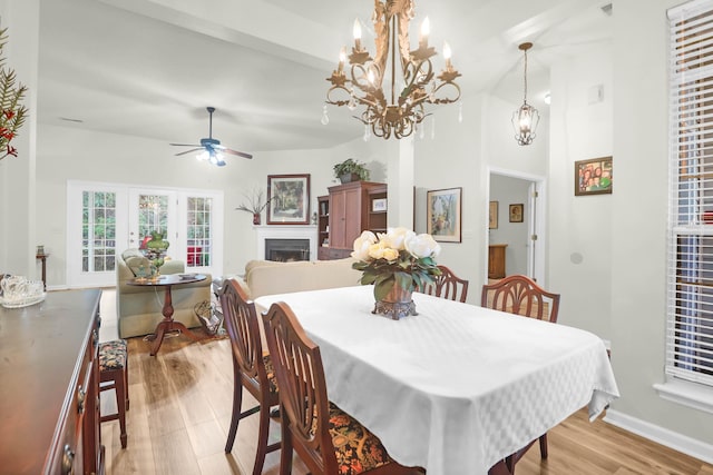 dining area featuring baseboards, high vaulted ceiling, light wood-style flooring, a fireplace, and ceiling fan with notable chandelier