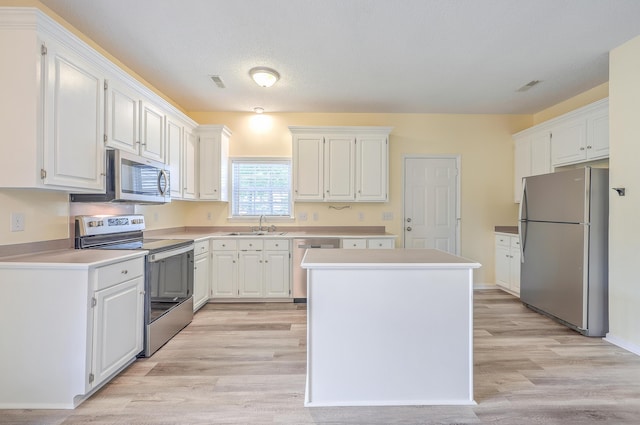 kitchen with stainless steel appliances, a sink, white cabinets, and a center island