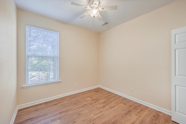 spare room with light wood-type flooring, ceiling fan, visible vents, and a textured ceiling