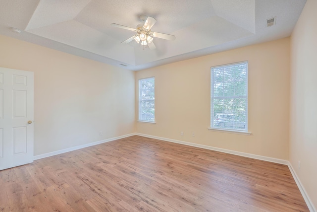empty room featuring a healthy amount of sunlight, baseboards, and a raised ceiling