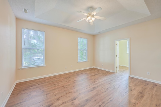 unfurnished room featuring light wood finished floors, baseboards, visible vents, a ceiling fan, and a tray ceiling