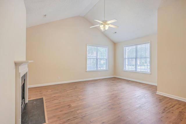 unfurnished living room with ceiling fan, a fireplace with flush hearth, wood finished floors, vaulted ceiling, and a textured ceiling