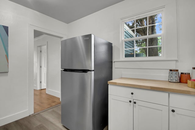 kitchen with white cabinets, butcher block countertops, stainless steel refrigerator, and light hardwood / wood-style flooring