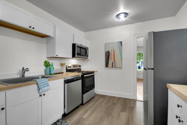 kitchen featuring wooden counters, stainless steel appliances, sink, light hardwood / wood-style flooring, and white cabinetry