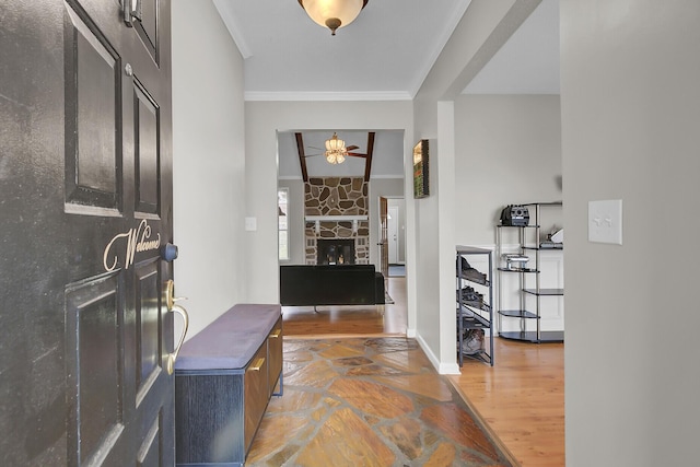 foyer entrance featuring a fireplace, ornamental molding, ceiling fan, wood finished floors, and baseboards