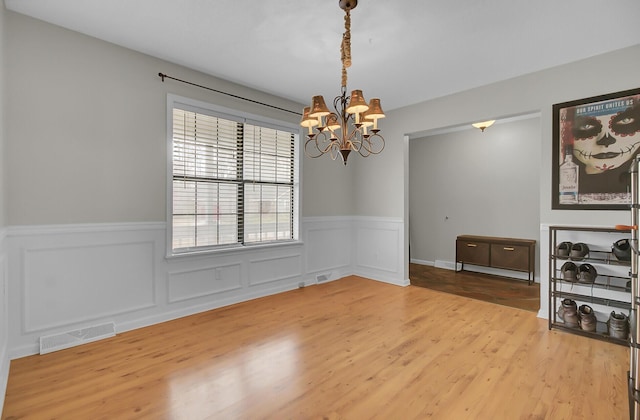 unfurnished dining area featuring visible vents, a chandelier, wood finished floors, and wainscoting