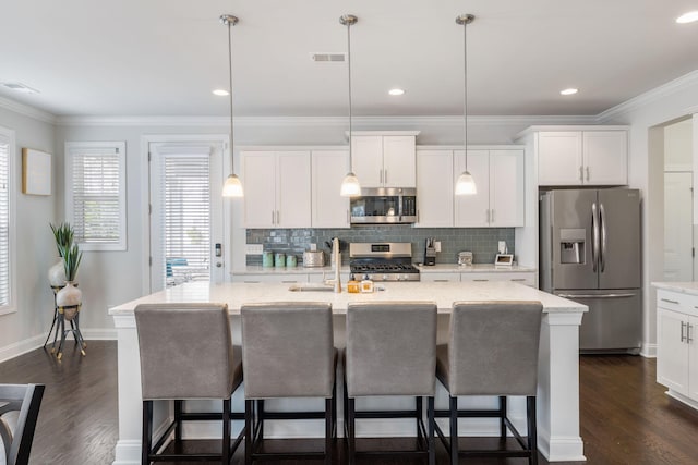 kitchen featuring stainless steel appliances, visible vents, ornamental molding, a sink, and a kitchen bar