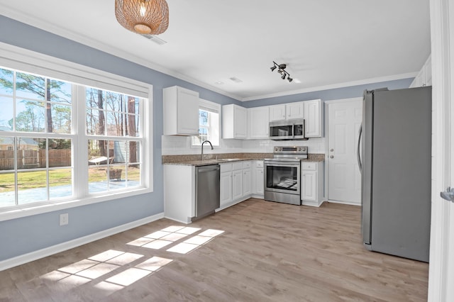 kitchen featuring light wood finished floors, ornamental molding, appliances with stainless steel finishes, white cabinetry, and backsplash