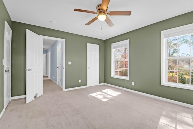 unfurnished bedroom with baseboards, multiple windows, light colored carpet, and ceiling fan