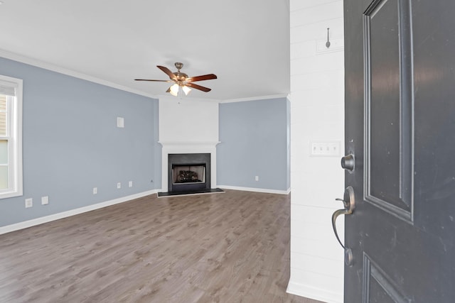 living area featuring a fireplace with raised hearth, a ceiling fan, wood finished floors, crown molding, and baseboards