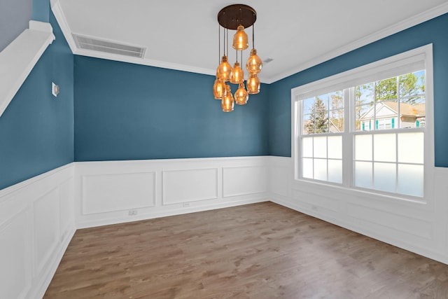 unfurnished dining area with wood finished floors, a wainscoted wall, visible vents, an inviting chandelier, and crown molding