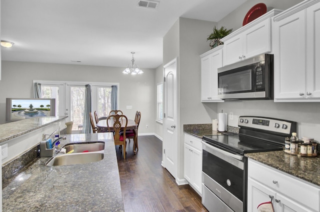 kitchen with white cabinets, appliances with stainless steel finishes, dark stone counters, sink, and a chandelier