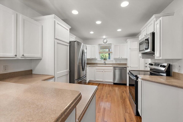 kitchen featuring appliances with stainless steel finishes, sink, light hardwood / wood-style floors, and white cabinets