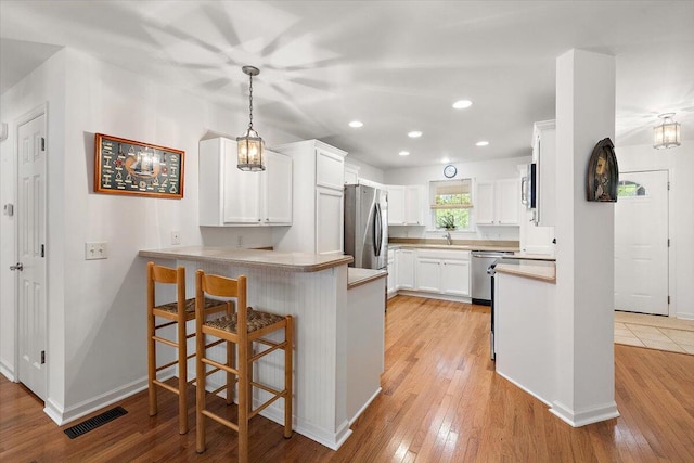 kitchen with white cabinets, kitchen peninsula, light hardwood / wood-style flooring, and a breakfast bar