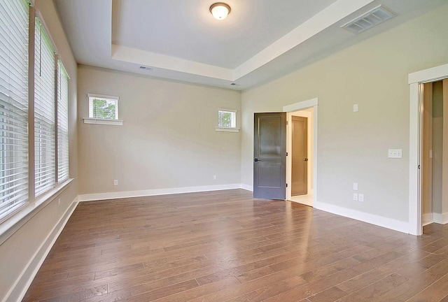 unfurnished room featuring a healthy amount of sunlight, dark hardwood / wood-style floors, and a tray ceiling