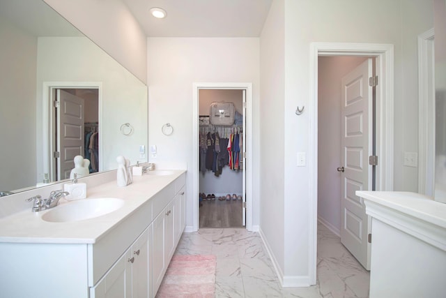 full bathroom with double vanity, marble finish floor, a walk in closet, and a sink