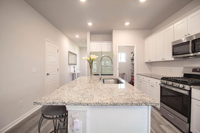 kitchen with a sink, light wood-style flooring, backsplash, white cabinetry, and appliances with stainless steel finishes