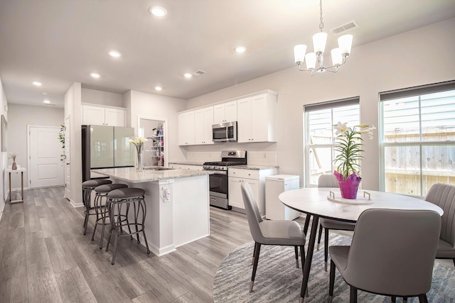 kitchen with appliances with stainless steel finishes, light wood-type flooring, visible vents, a chandelier, and an island with sink
