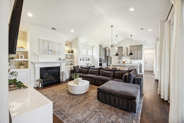 living area featuring dark wood-type flooring, lofted ceiling, a fireplace with flush hearth, a chandelier, and recessed lighting