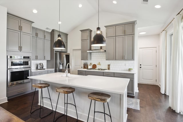kitchen featuring gray cabinetry, stainless steel appliances, vaulted ceiling, tasteful backsplash, and a breakfast bar
