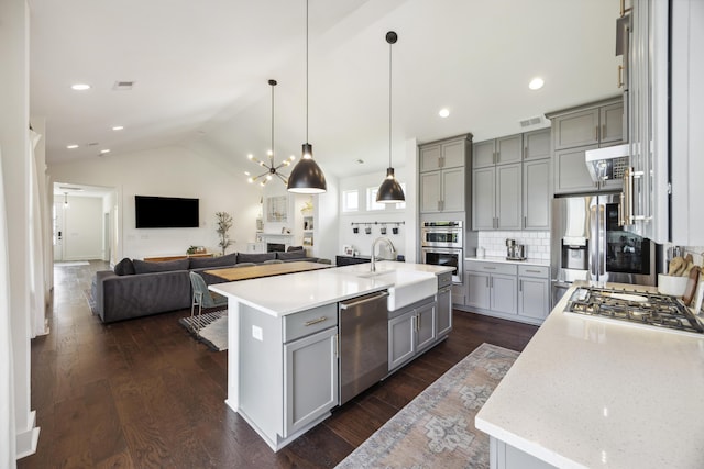 kitchen featuring gray cabinetry, stainless steel appliances, a sink, open floor plan, and decorative backsplash