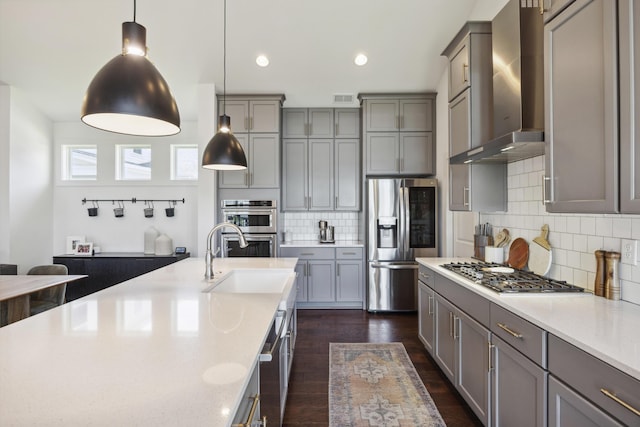 kitchen with stainless steel appliances, wall chimney exhaust hood, gray cabinetry, a sink, and recessed lighting