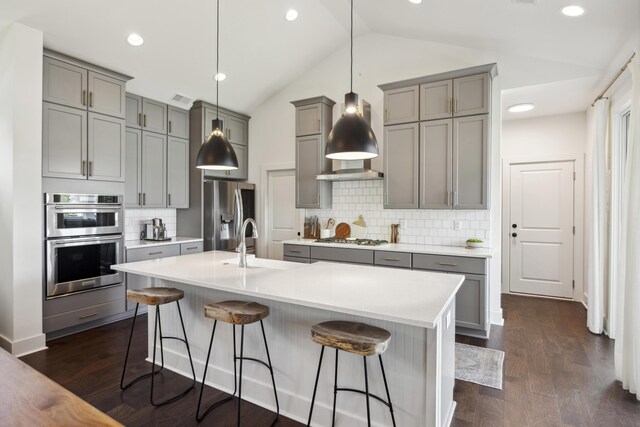 kitchen featuring gray cabinetry, appliances with stainless steel finishes, a sink, vaulted ceiling, and a kitchen breakfast bar