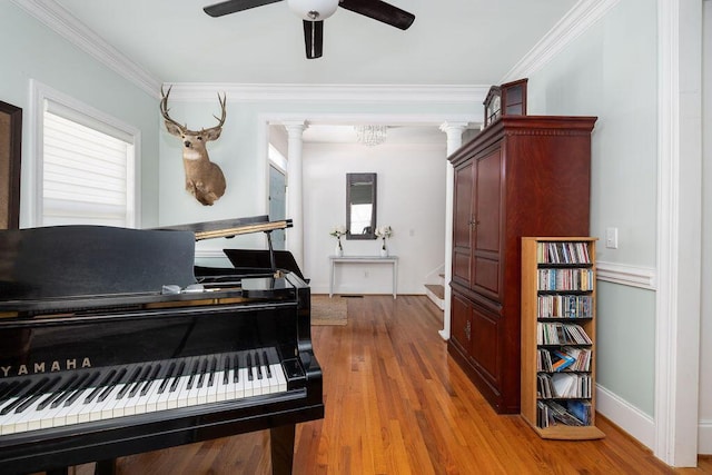living area with a ceiling fan, baseboards, ornamental molding, wood finished floors, and ornate columns