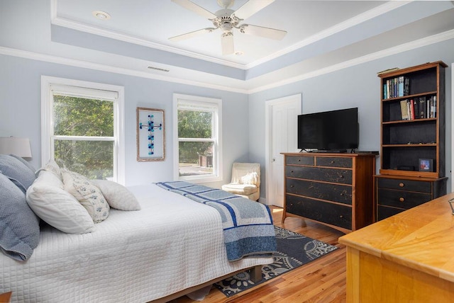 bedroom with wood finished floors, a tray ceiling, visible vents, ceiling fan, and ornamental molding