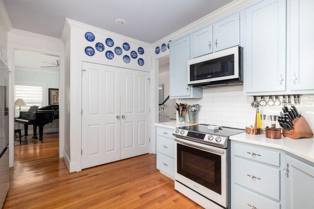 kitchen with white microwave, stainless steel electric range, light wood-type flooring, crown molding, and backsplash
