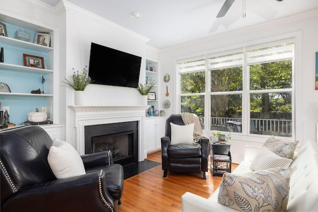 living room featuring light wood finished floors, ornamental molding, a ceiling fan, and built in shelves