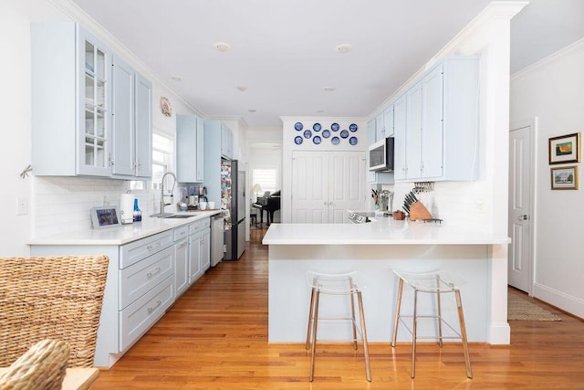 kitchen with a sink, a peninsula, decorative backsplash, stainless steel appliances, and light wood-type flooring
