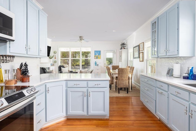 kitchen featuring a peninsula, stainless steel range with electric stovetop, white microwave, decorative backsplash, and light wood-style floors