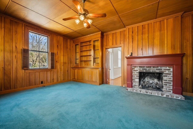 unfurnished living room featuring a brick fireplace, wooden ceiling, wooden walls, carpet floors, and ceiling fan