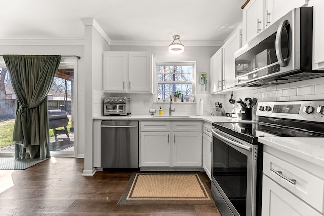 kitchen with a sink, backsplash, dark wood finished floors, appliances with stainless steel finishes, and light countertops