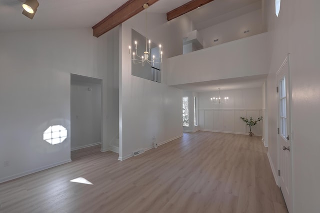 unfurnished living room featuring an inviting chandelier, high vaulted ceiling, and light hardwood / wood-style flooring