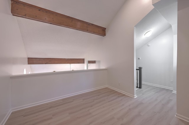 unfurnished room with lofted ceiling with beams and light wood-type flooring