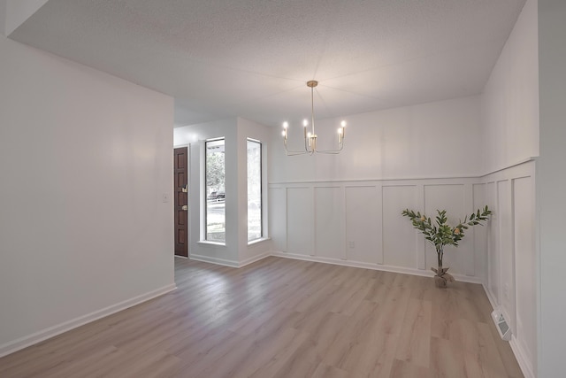 unfurnished dining area featuring a notable chandelier, light wood-type flooring, and a textured ceiling