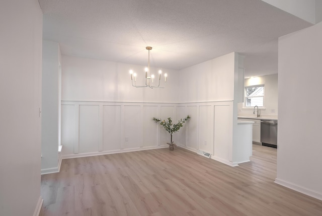 unfurnished dining area featuring a chandelier, a textured ceiling, light wood-type flooring, and sink