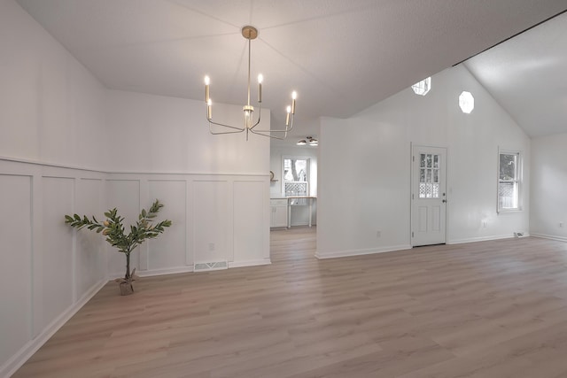 unfurnished dining area featuring high vaulted ceiling, a chandelier, and light wood-type flooring