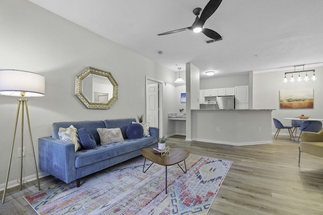 living area with ceiling fan, light wood finished floors, visible vents, and baseboards