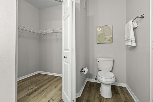 bathroom featuring a walk in closet, baseboards, toilet, and wood finished floors