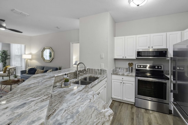 kitchen featuring open floor plan, stainless steel appliances, a sink, and light stone countertops