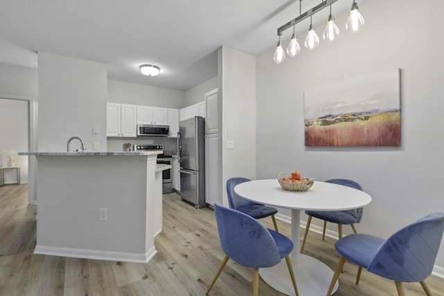 kitchen with stainless steel appliances, a sink, white cabinetry, baseboards, and light wood-type flooring