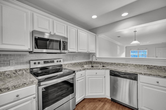 kitchen with tasteful backsplash, appliances with stainless steel finishes, white cabinetry, a sink, and wood finished floors