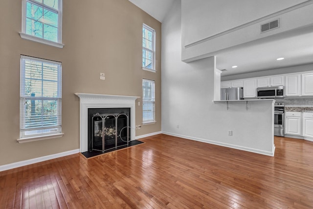 unfurnished living room with wood-type flooring, visible vents, a fireplace, and baseboards