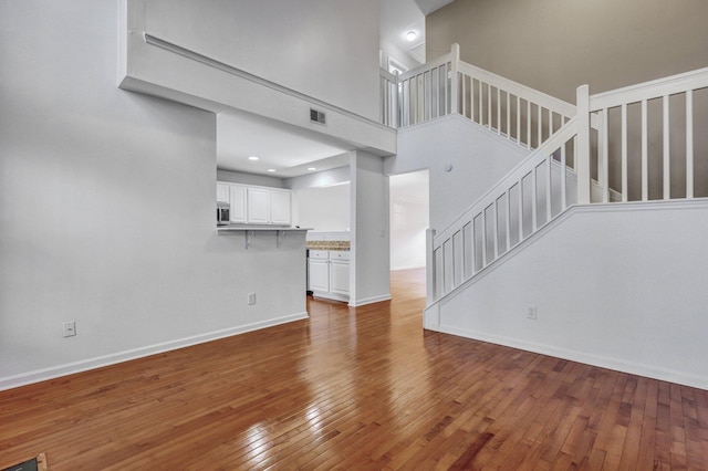 unfurnished living room featuring hardwood / wood-style flooring, visible vents, stairway, and baseboards