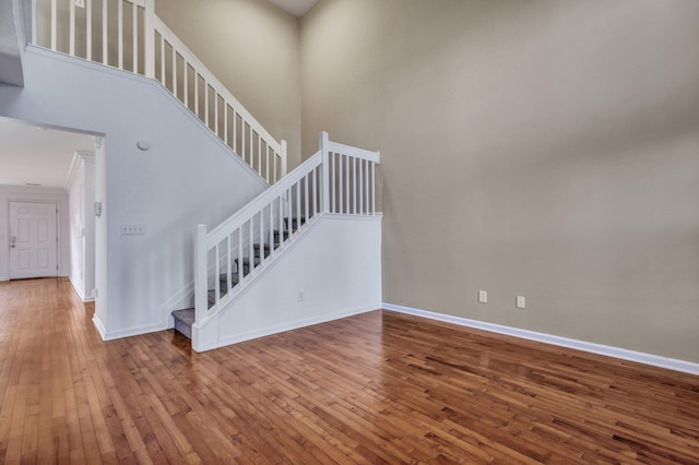 stairs featuring baseboards, a towering ceiling, and hardwood / wood-style floors